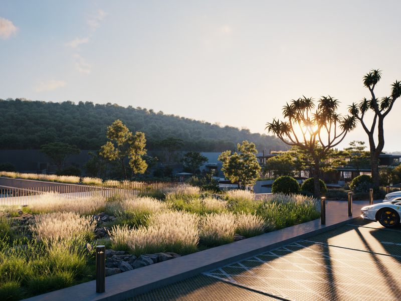 A modern landscaped exterior area featuring a paved parking space, decorative grasses, and integrated bollard lighting at sunset.