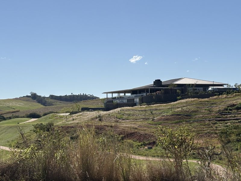 A modern residence featuring stone cladding and a metal roof, situated on a landscaped hillside with a spacious covered patio and glass balustrade.