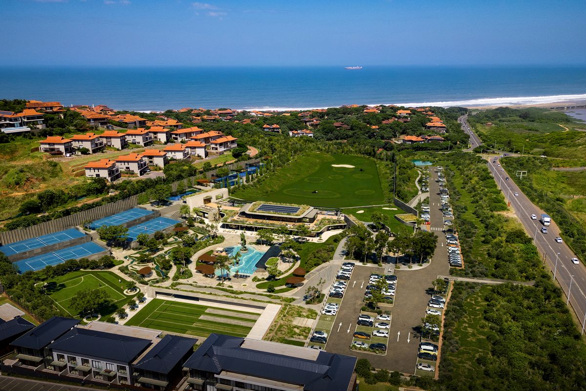 Aerial view of a residential estate featuring a swimming pool, tennis courts, golf course, and extensive parking facilities near the coastline.