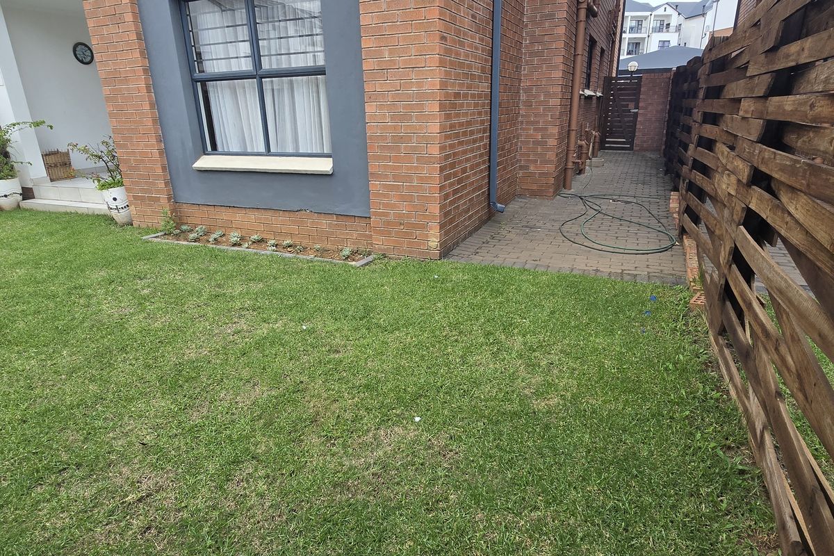 A private rear garden area featuring a well-maintained lawn, paved side walkway, and timber slat boundary fencing.