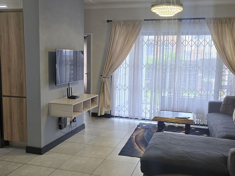 Open-plan living area featuring a modern kitchen with built-in cabinetry and appliances, flowing into a comfortable lounge with access to a patio.
