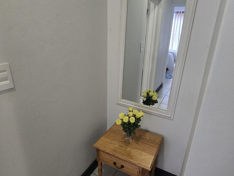 A bright hallway area featuring neutral wall finishes, tiled flooring, and a wall-mounted mirror, providing a clean transition between living spaces.