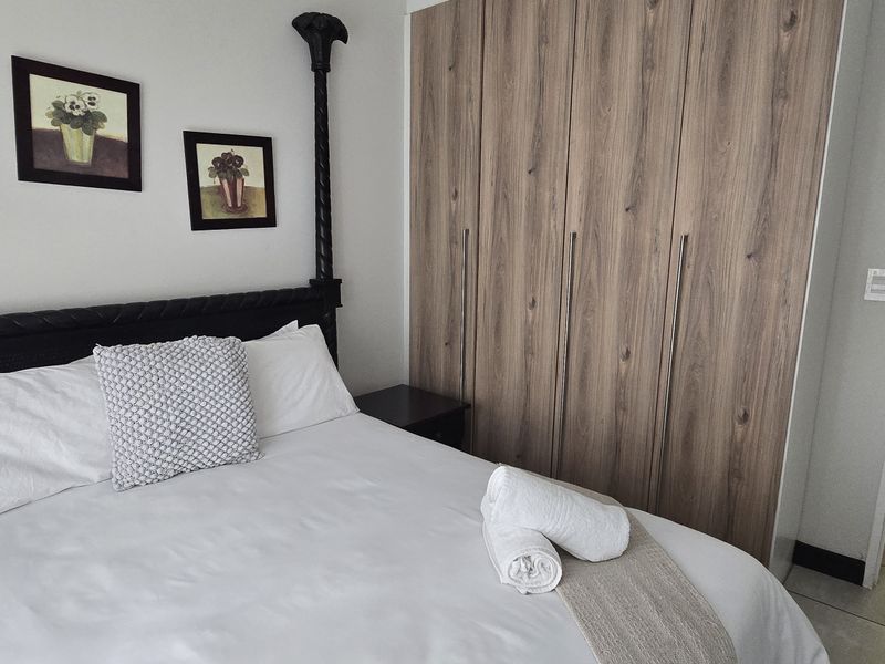 A well-maintained bedroom featuring modern wood-finish built-in cupboards and neutral tiled flooring, offering a clean and functional living space.