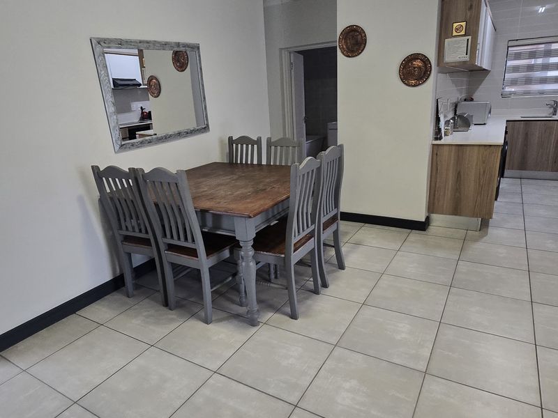 An open-plan living and dining area featuring tiled flooring, neutral walls, and a functional kitchen with modern wood-finish cabinetry and integrated appliances.