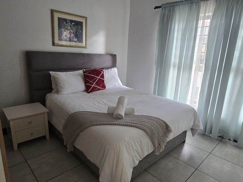 A well-maintained bedroom featuring neutral tiled flooring and large windows with curtain tracks, providing a bright and comfortable living space.