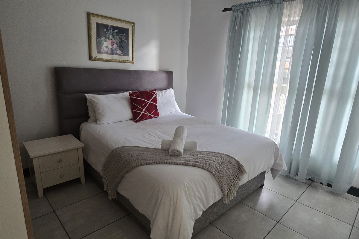A well-maintained bedroom featuring neutral tiled flooring and large windows with curtain tracks, providing a bright and comfortable living space.