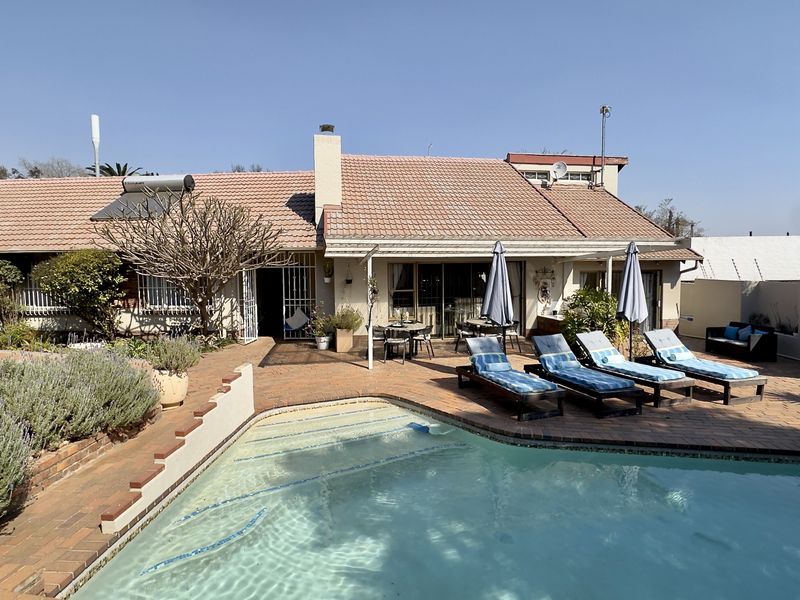 Rear exterior view featuring a swimming pool, brick paved patio area, and a well-maintained garden with a tiled roof residence.