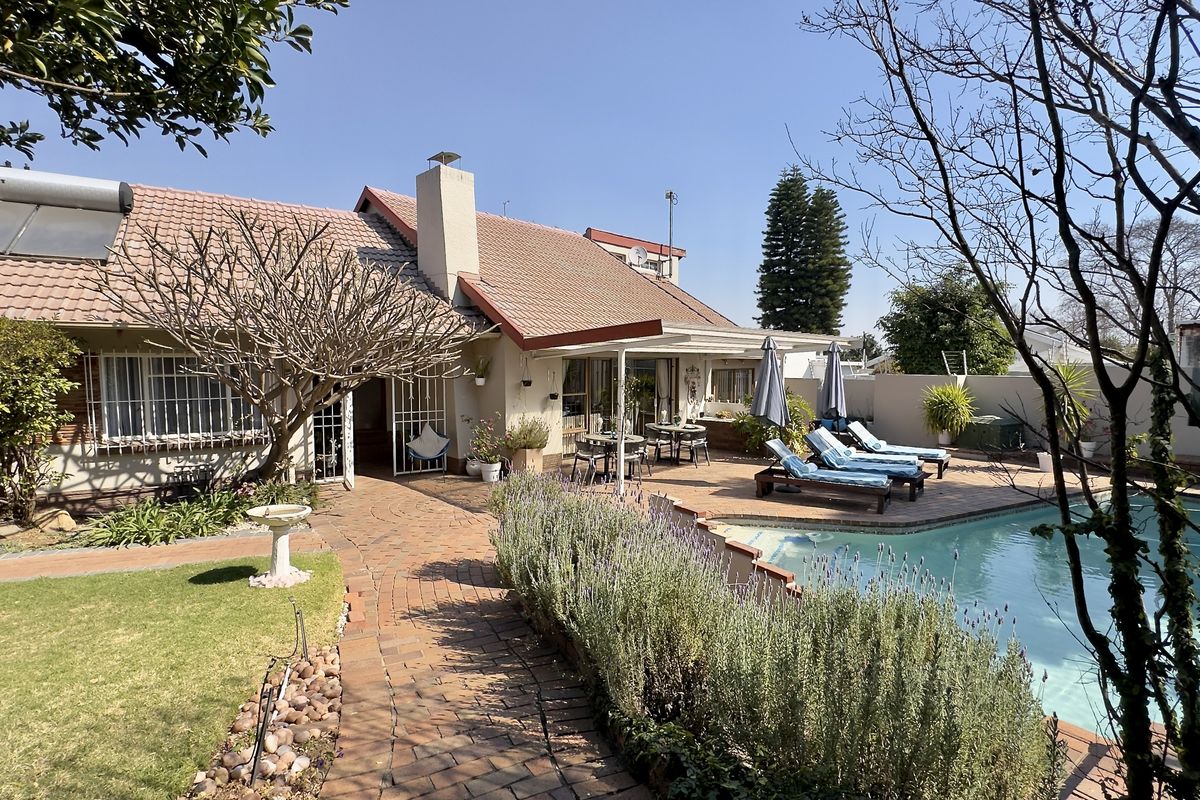 Rear exterior view featuring a swimming pool, brick paved patio area, and established garden with a tiled roof house and solar water heating system.