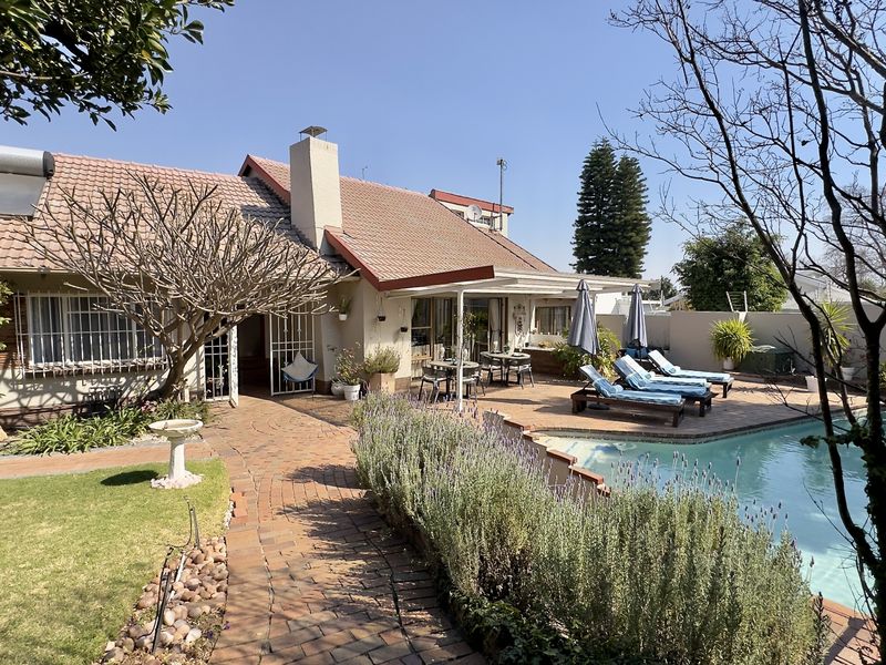 Rear exterior view featuring a swimming pool, brick paved patio area, and established garden with a tiled roof house and solar water heating system.