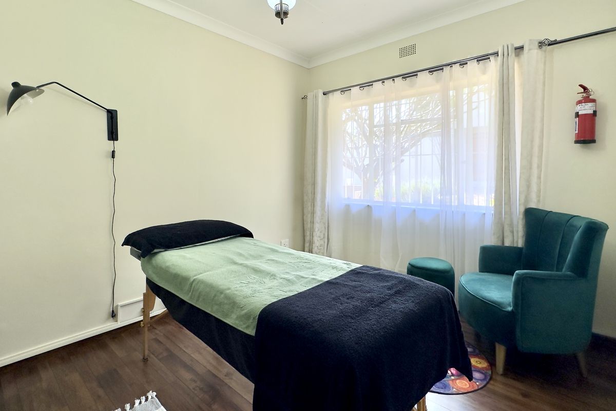 A functional bedroom space featuring laminate flooring, coving, and a wall-mounted light fixture, currently utilized as a treatment room.