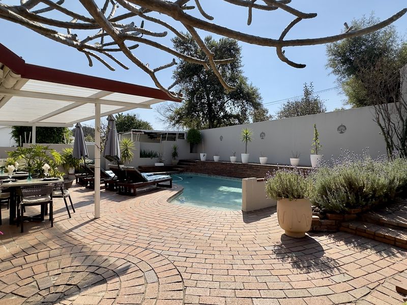 Outdoor entertainment area featuring a swimming pool, brick-paved patio, and a covered pergola, ideal for relaxation and hosting guests.
