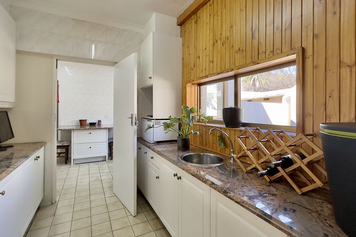 A functional kitchen featuring granite countertops, white cabinetry, and timber wall paneling, with an adjacent scullery area visible through the doorway.