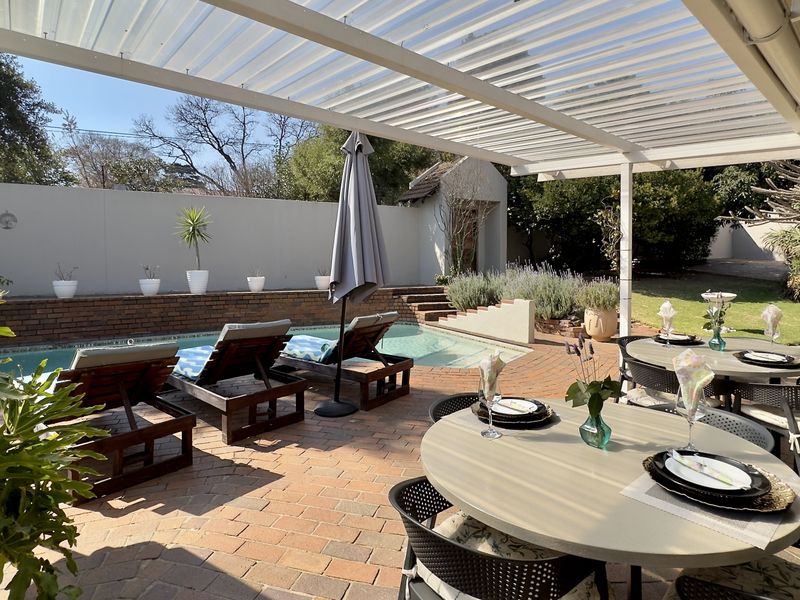A well-maintained outdoor entertainment area featuring a swimming pool, brick paving, and a covered patio structure, ideal for alfresco dining and relaxation.