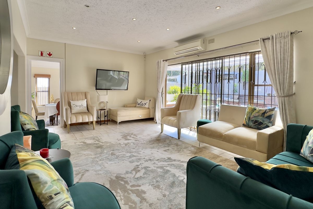 Spacious living room featuring tiled flooring, recessed downlighting, and a wall-mounted air conditioning unit, with direct access to the outdoor area through security gates.