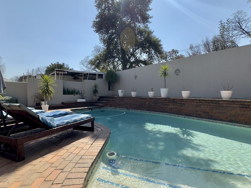 A well-maintained swimming pool area featuring brick paving, a raised brick retaining wall, and a solid boundary wall.