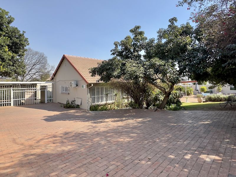 Front exterior view of the house featuring a spacious paved driveway, security gate, and established garden surroundings.