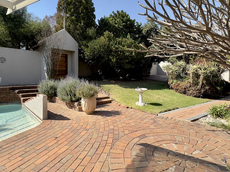 A well-maintained outdoor pool area featuring brick paving, landscaped garden beds, and a boundary wall, providing a pleasant space for relaxation.