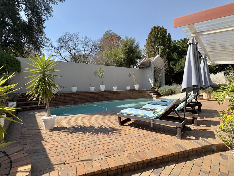 Outdoor pool area featuring a swimming pool, brick paved surround, and a covered patio structure, set within a private walled garden.