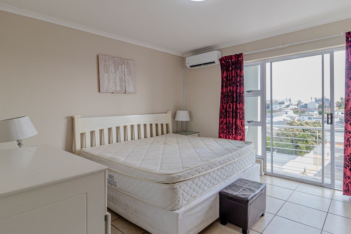 A bedroom featuring tiled flooring, a wall-mounted air conditioning unit, and sliding glass doors providing access to a balcony with neighborhood views.