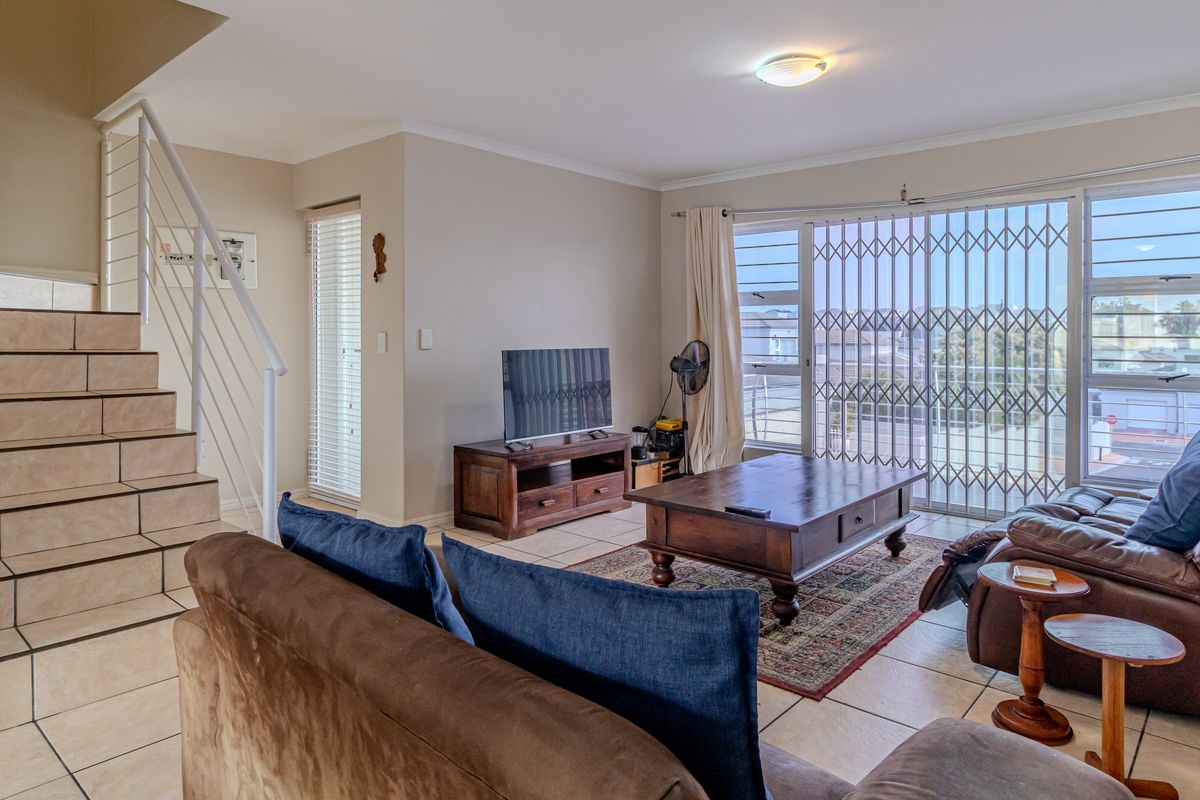 Spacious living room featuring tiled flooring, a staircase with a metal balustrade, and a sliding glass door leading to an outdoor area with security gates.