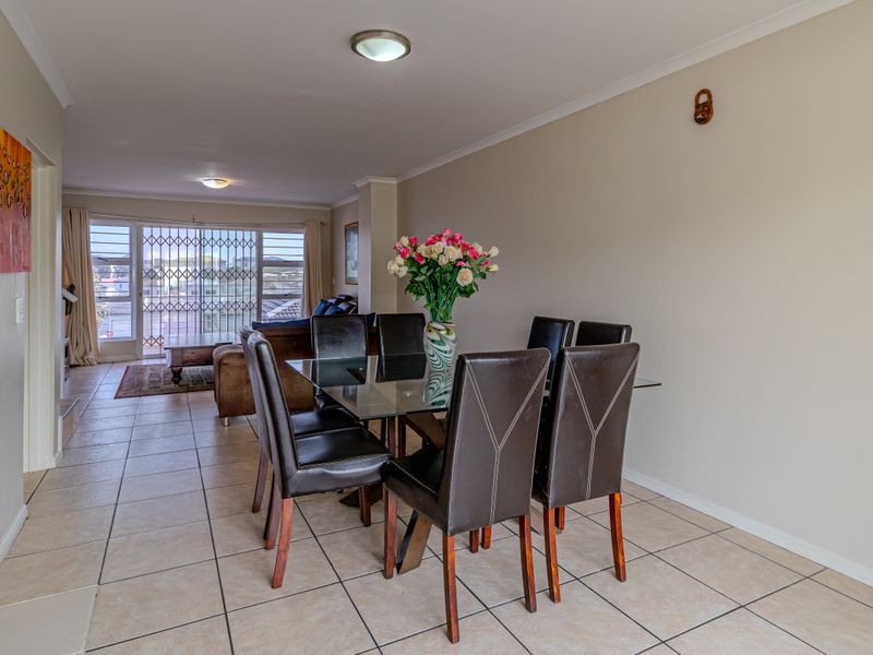An open-plan living and dining area featuring neutral tiled flooring, coved cornicing, and a sliding glass door leading to an outdoor space with security gate.