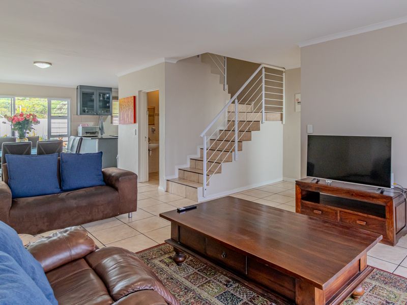 Open-plan living area featuring tiled flooring, a central staircase with metal balustrades, and an integrated kitchen space with neutral wall finishes.