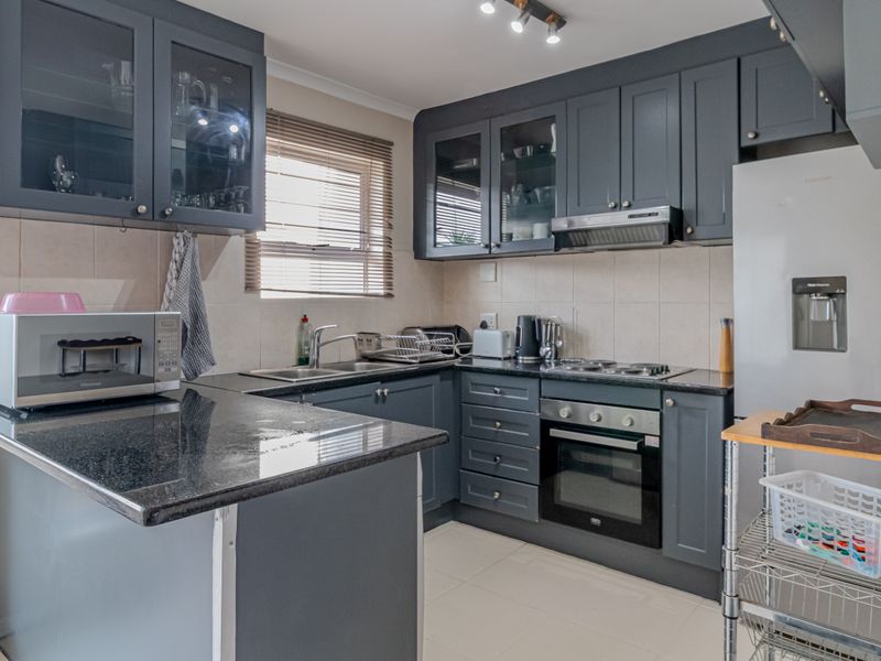 Modern kitchen featuring dark grey cabinetry, granite countertops, built-in oven, electric hob, and a tiled backsplash with neutral floor tiles.