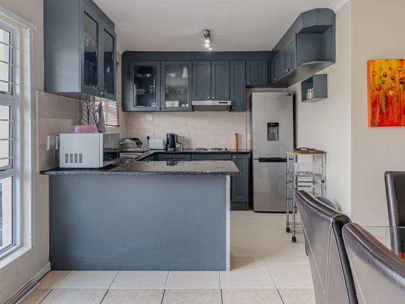 A functional kitchen featuring dark cabinetry, granite countertops, and tiled flooring, with an open-plan layout connecting to the dining area.