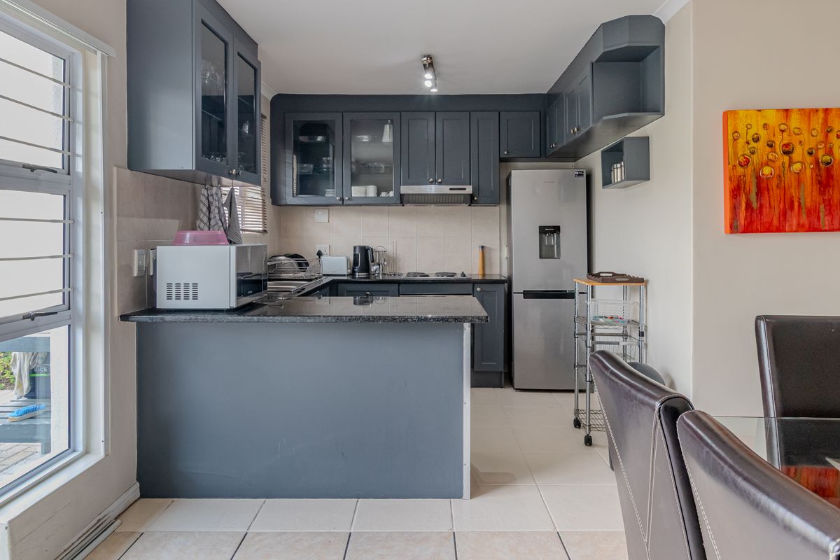 A functional kitchen featuring dark cabinetry, granite countertops, and tiled flooring, with an open-plan layout connecting to the dining area.