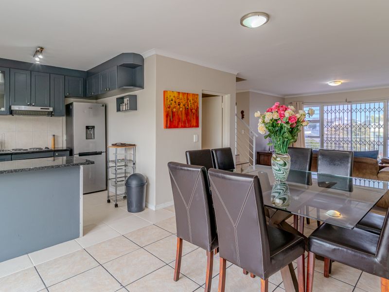 Open-plan kitchen and dining area featuring dark cabinetry, granite countertops, and ceramic floor tiles, leading to a bright living space with sliding door access.