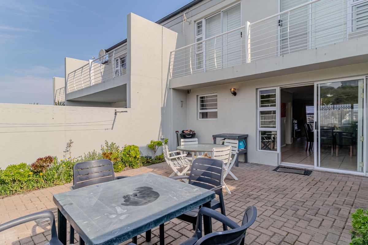 Rear exterior view of the townhouse featuring a paved patio area, sliding door access to the interior, and an upper-level balcony with metal railings.
