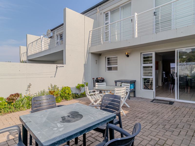 Rear exterior view of the townhouse featuring a paved patio area, sliding door access to the interior, and an upper-level balcony with metal railings.