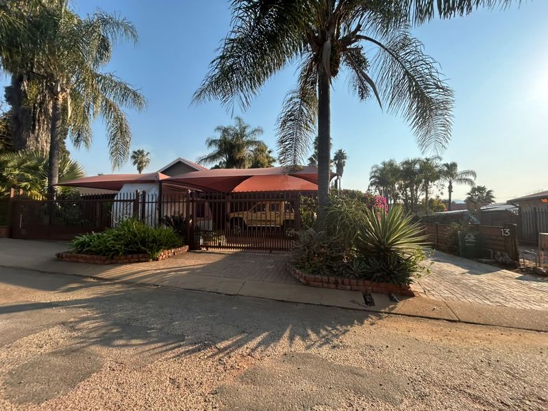 Front exterior view of the property featuring a paved driveway, secure metal gate, and shade sail structure over the parking area.