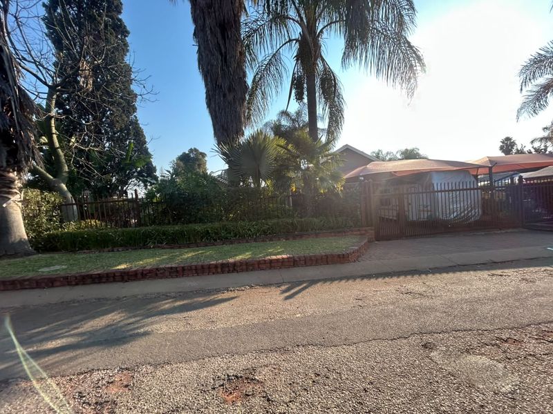 Street view of the property frontage featuring metal perimeter fencing, a brick-edged garden bed, and a covered carport area.