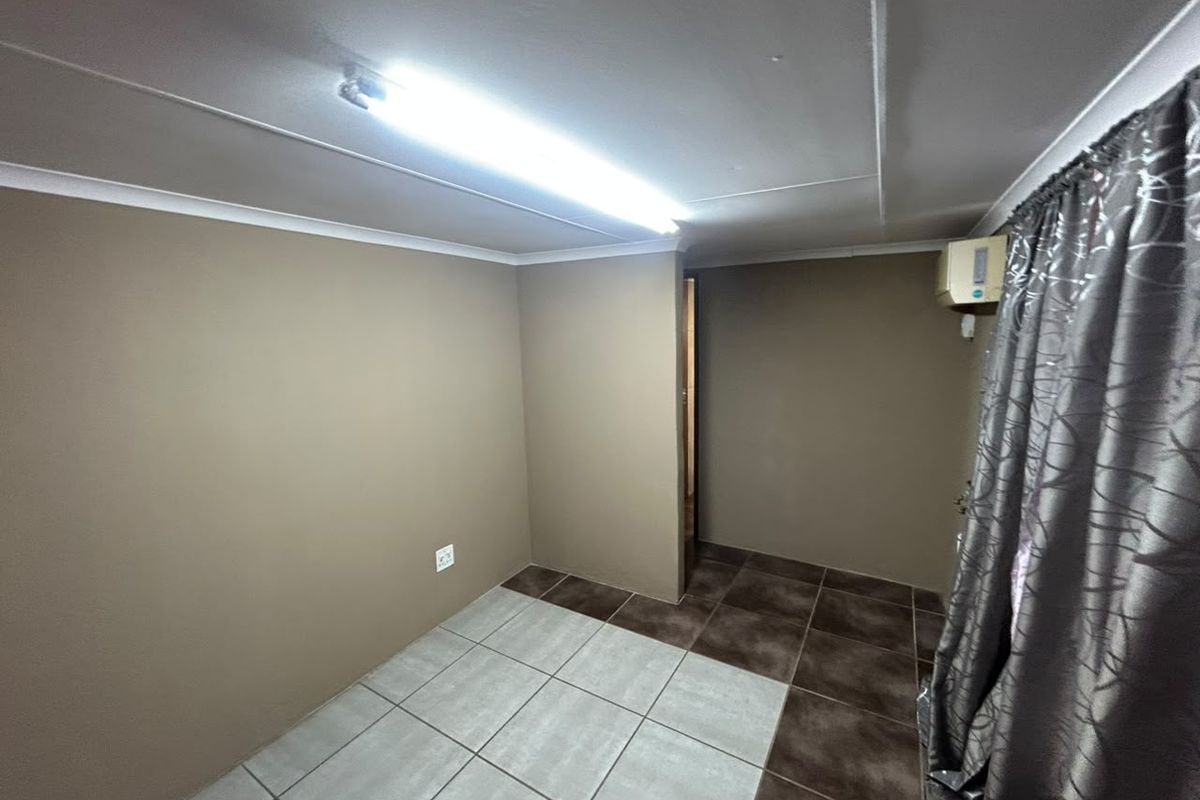 An empty bedroom featuring tiled flooring, a wall-mounted air conditioning unit, and a fluorescent light fixture.