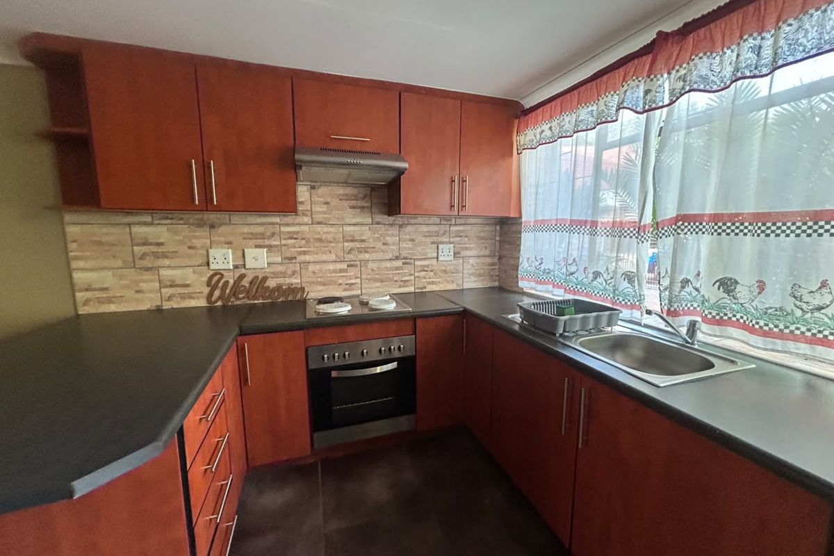 A functional kitchen featuring warm-toned wooden cabinetry, dark laminate countertops, a built-in oven with hob, and a tiled backsplash.