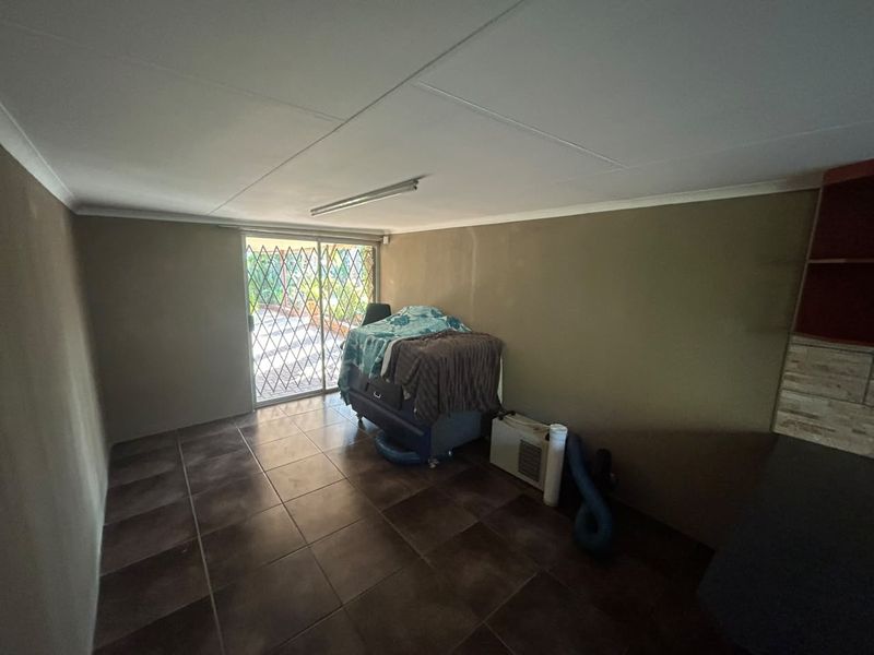A simple living area featuring dark floor tiles, a sliding glass door with security gate, and basic overhead lighting.