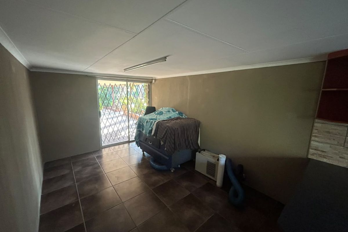 A simple living area featuring dark floor tiles, a sliding glass door with security gate, and basic overhead lighting.
