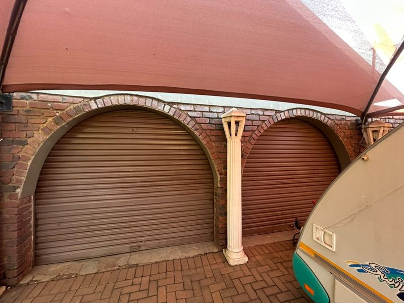 Double garage featuring distinctive brick archways and roller shutter doors, protected by an overhead shade sail structure.