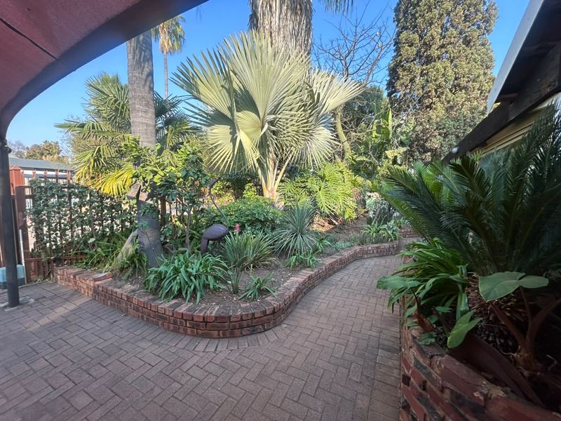 A covered patio area featuring brick paving and a curved brick retaining wall, surrounded by established garden landscaping.