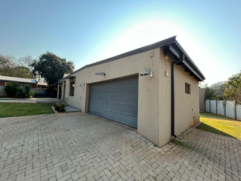 A detached garage building featuring a roller shutter door, paved driveway, and exterior lighting, situated on a well-maintained residential property.