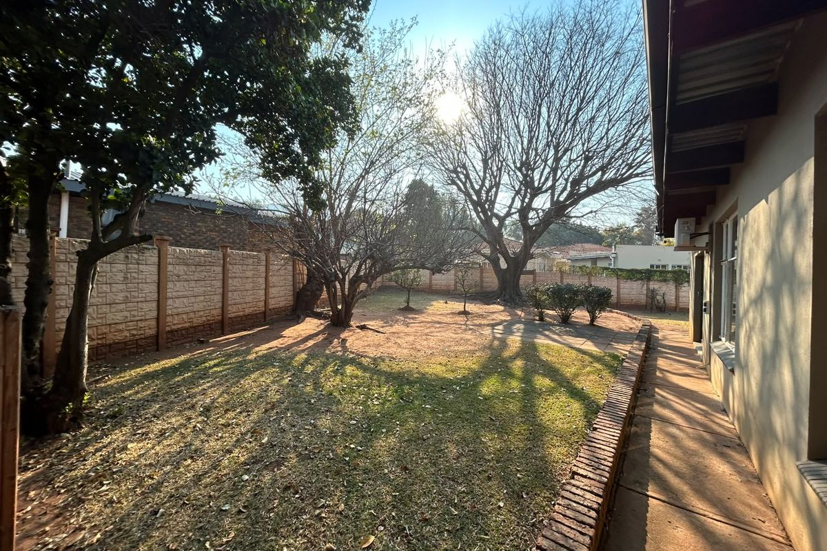 A spacious rear garden featuring a paved walkway, brick edging, and established trees, enclosed by a precast concrete boundary wall.