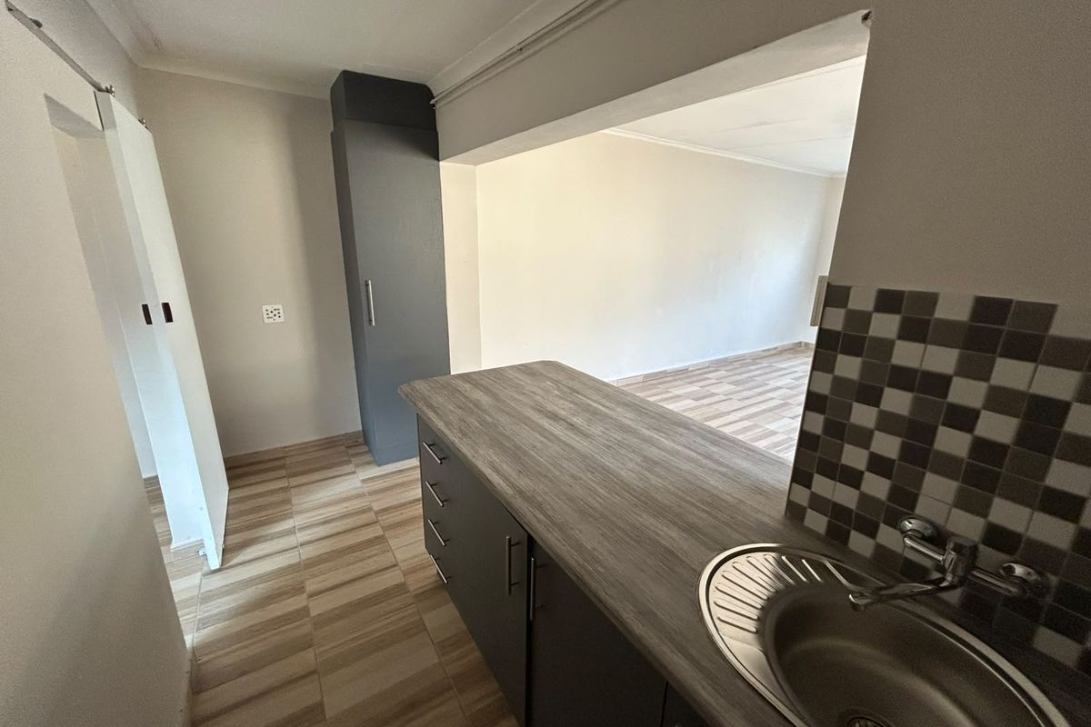 A compact kitchen area featuring modern grey cabinetry, wood-look laminate countertops, a stainless steel sink, and a decorative tiled splashback.