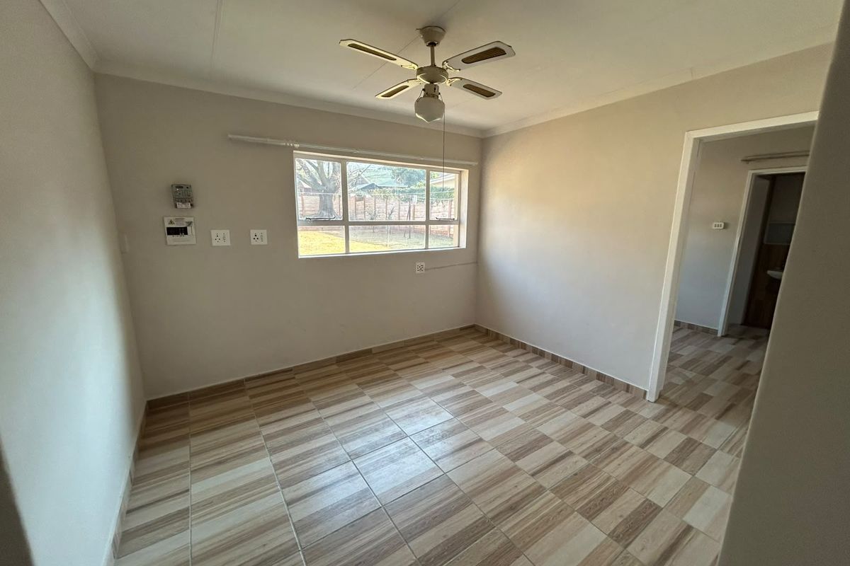 A bright, empty living room featuring neutral walls, tiled flooring, and a ceiling fan, offering a clean canvas for personalization.