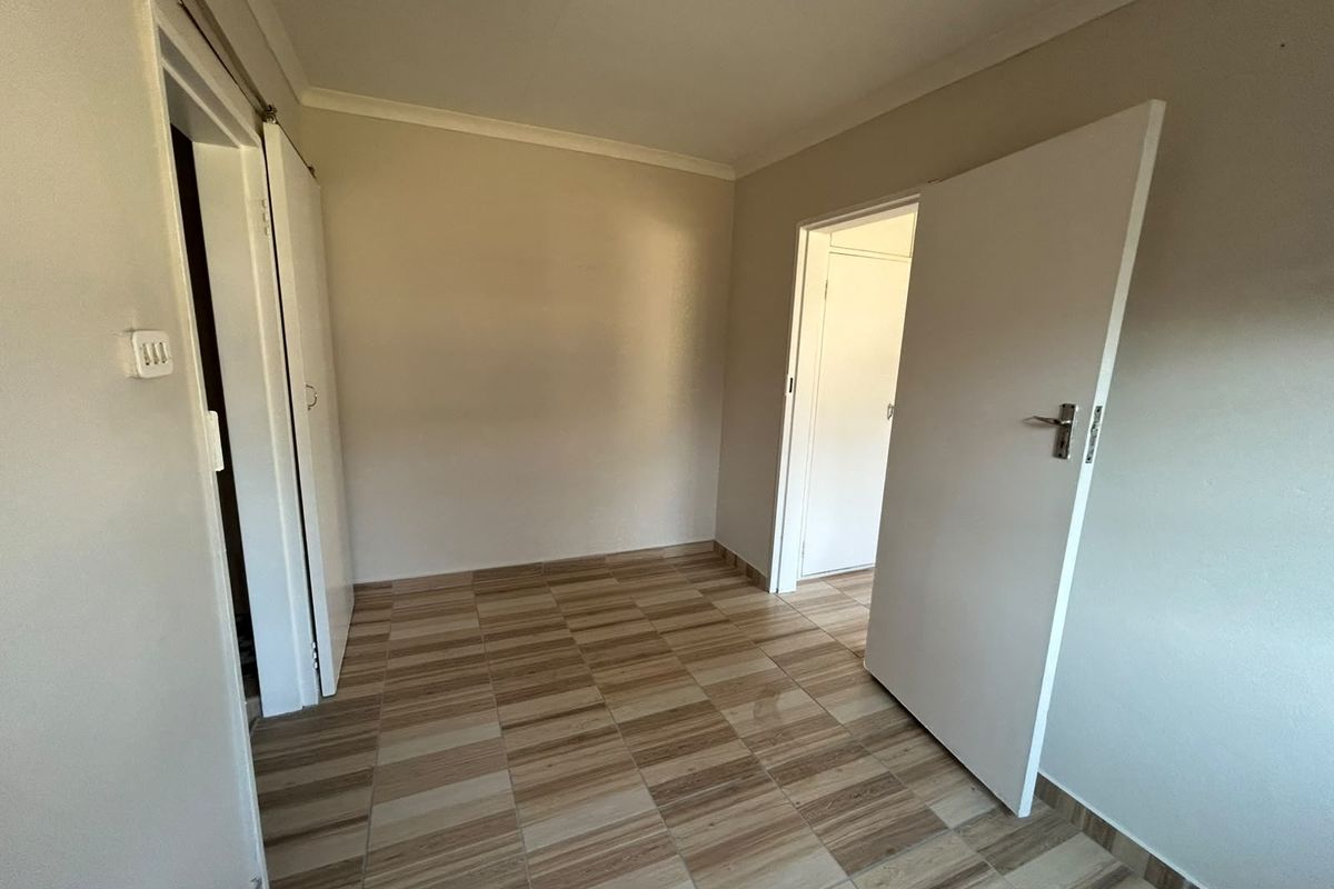 An empty bedroom featuring tiled flooring, built-in cupboards, and neutral wall finishes, providing a clean canvas for personalization.