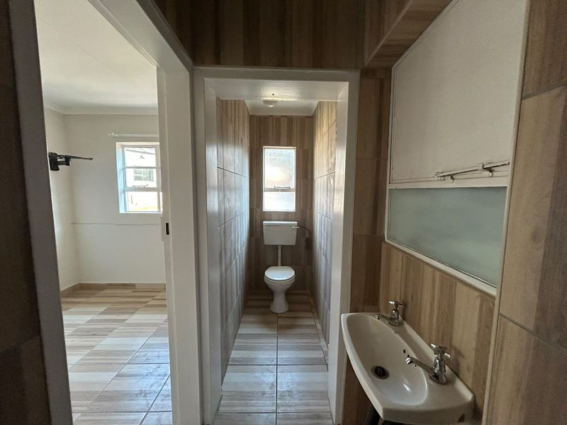 A functional bathroom featuring a wall-mounted basin, toilet, and tiled finishes, offering a clean, neutral space ready for potential cosmetic updates.