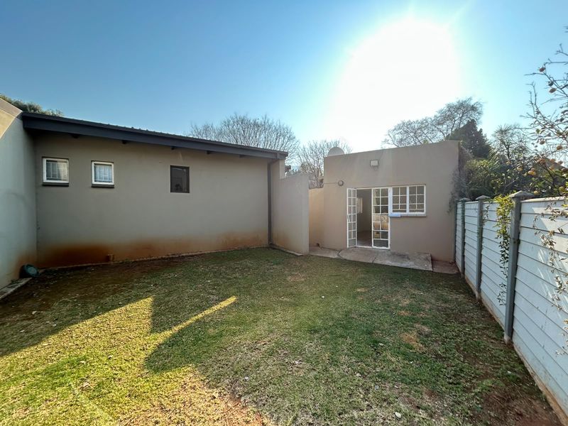 A rear exterior view of the property featuring a small lawn area, precast boundary wall, and access to the building via french doors.