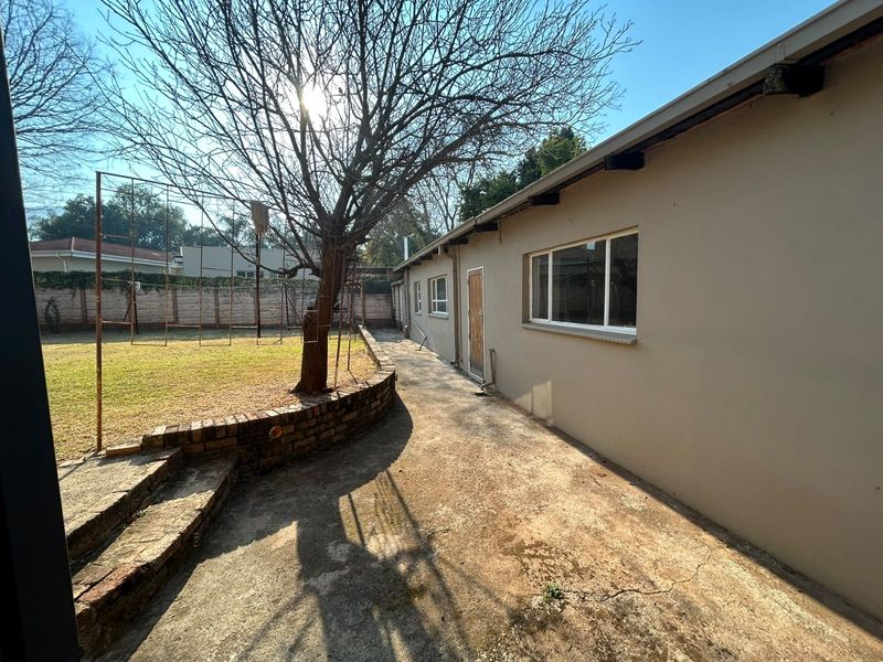 Rear exterior view of the property featuring a concrete pathway, brick retaining wall, and a spacious garden area with perimeter walling.