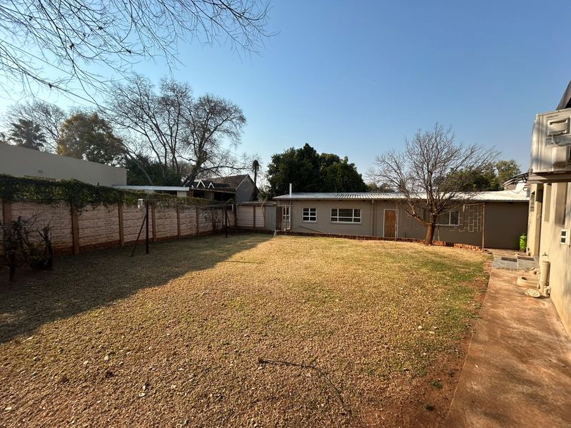 A spacious rear garden featuring a large lawn area, concrete pathway, and perimeter boundary wall, providing a private outdoor space for the property.