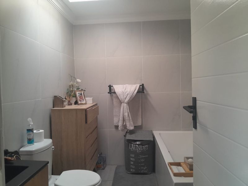A modern bathroom featuring neutral wall tiles, a built-in bathtub, and a vanity, presenting a clean and functional space.